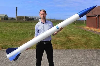 Daniel Innes, in a field, holding a rocket 